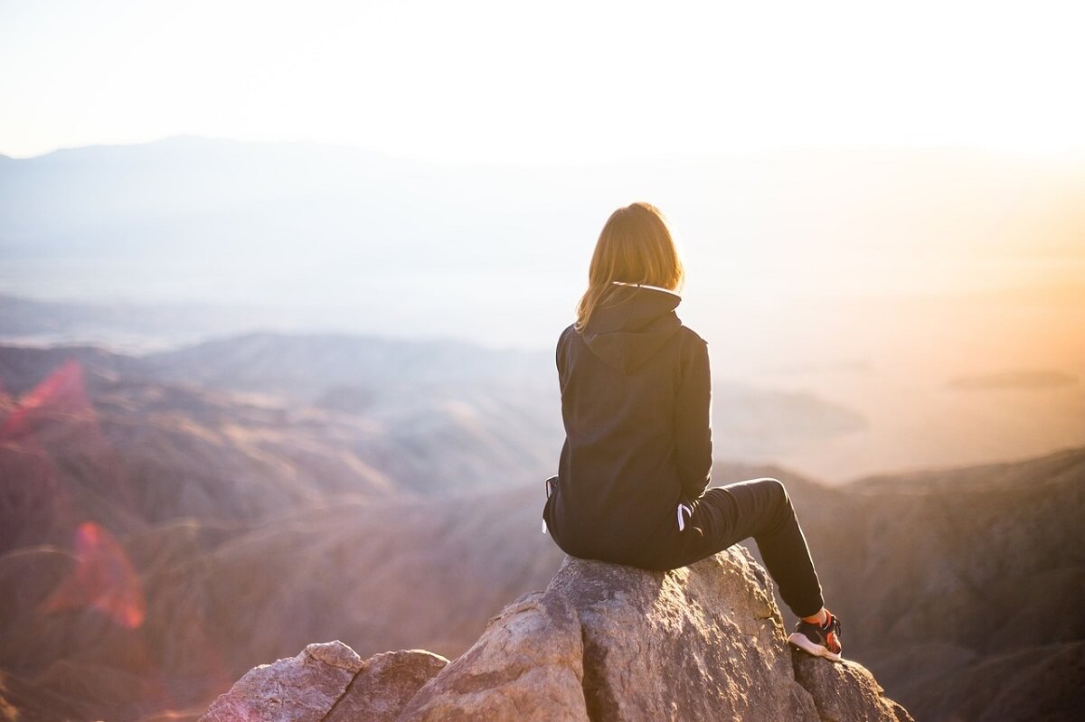 Kobieta siedzi tyłem do obiektywu na szczycie góry