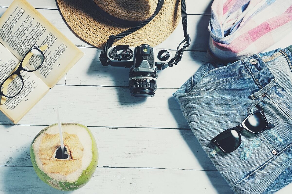 Rzeczy przydatne w podróży spodnie i okulary przeciwsłoneczne, aparat fotograficzny, kapelusz, książka i drink w kokosie
