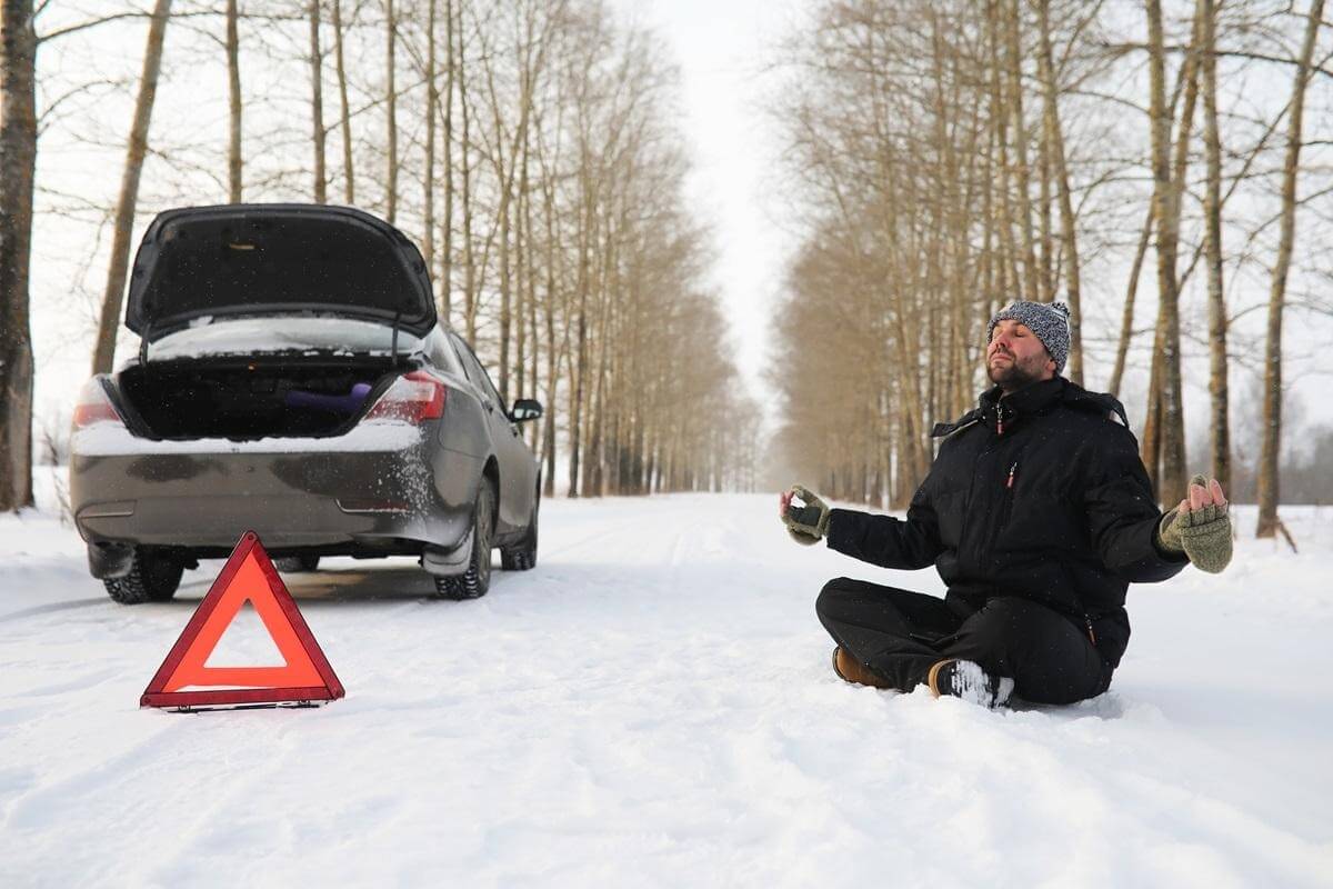 śnieg, samochód z otwartym bagażnikiem, mężczyzna siedzi na śniegu, trójkąt ostrzegawczy