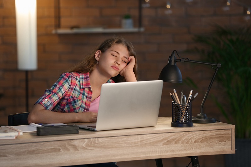 Zmęczona nastolatka odrabiająca pracę domową późnym wieczorem przed komputerem