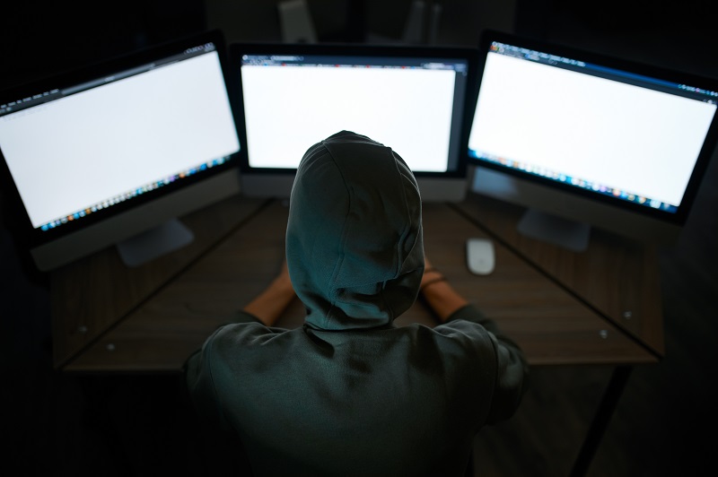 Haker internetowy w kapturze siedzi przy monitorach