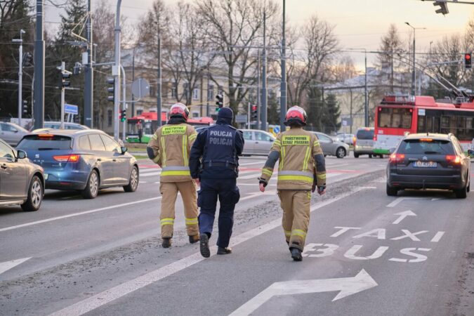 Dwóch strażaków i policjant idą wzdłuż ścieżki z betonu na jezdni