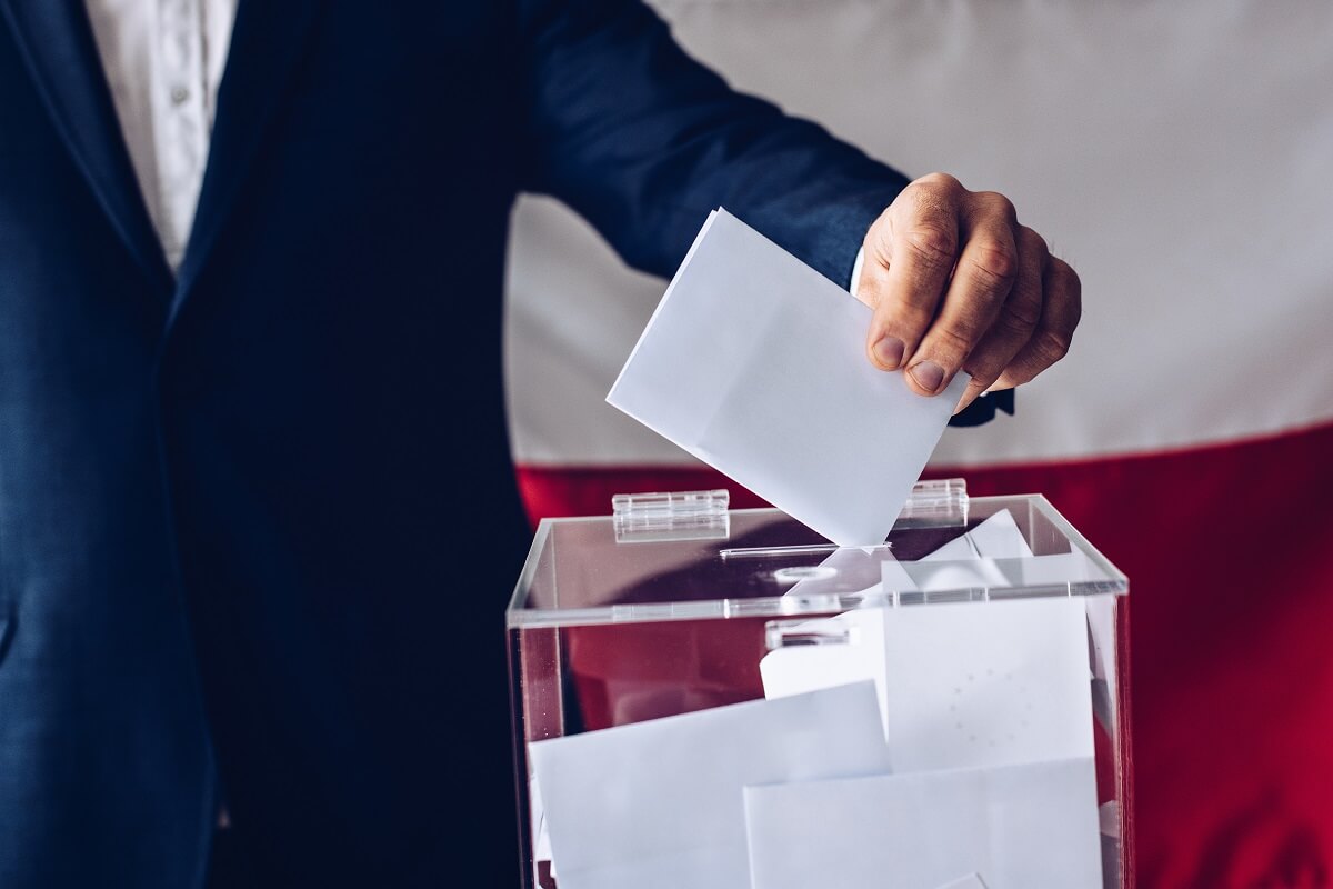 Mężczyzna w garniturze wrzucający kartkę z oddanym głosem do urny wyborczej