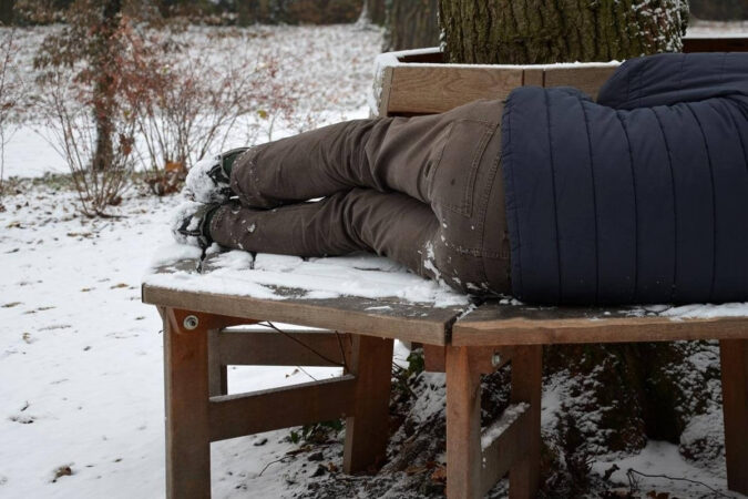 człowiek leży na ławce ze śniegiem