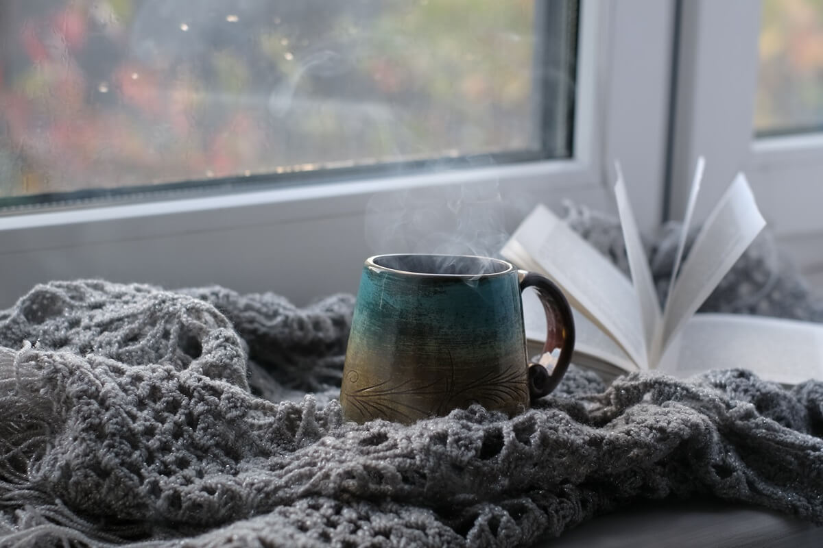 parująca filiżanka kawy na tle okna w deszczowy dzień. przytulna atmosfera, w chłodne dni